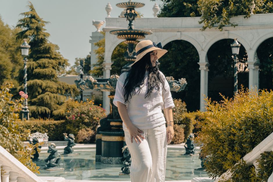 Woman standing near a fountain in a scenic garden setting.