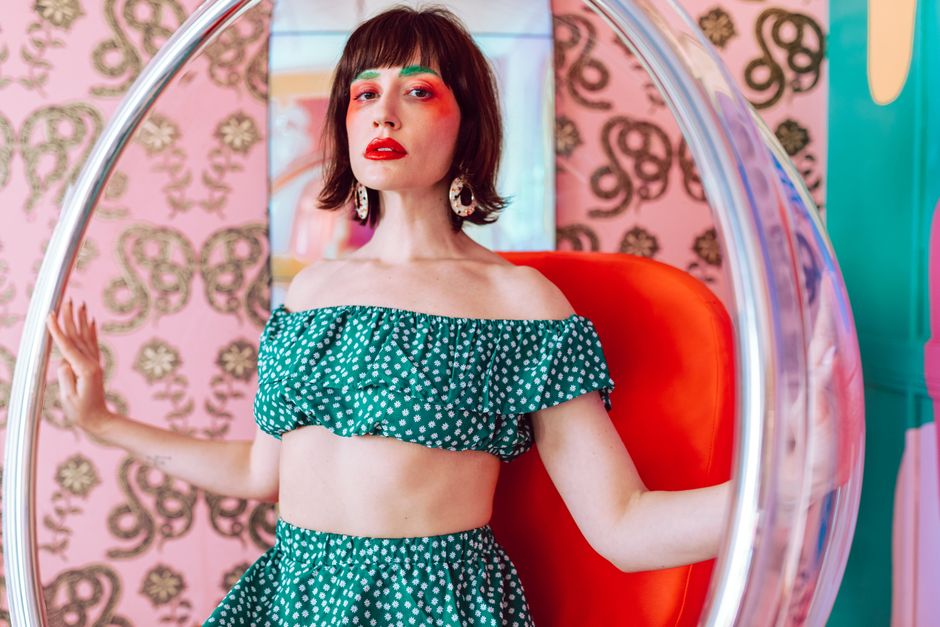 Colorful portrait featuring a woman in bold makeup and stylish outfit seated in a modern chair.