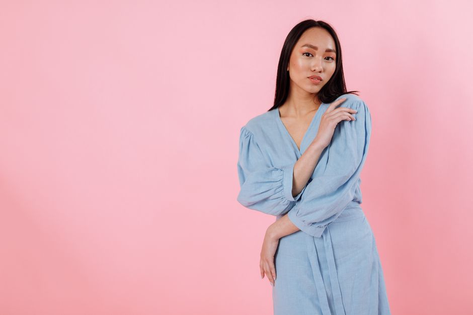 Studio portrait of a woman in a blue dress posing on a pink background