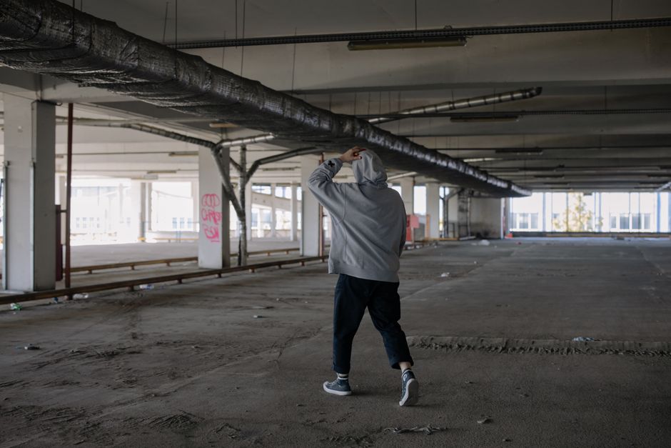 A lone figure in a grey hoodie walks through a deserted, industrial building, emphasizing urban exploration.