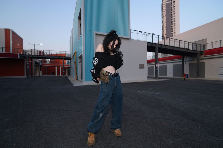 A stylish woman poses in an urban setting with colorful modern architecture.