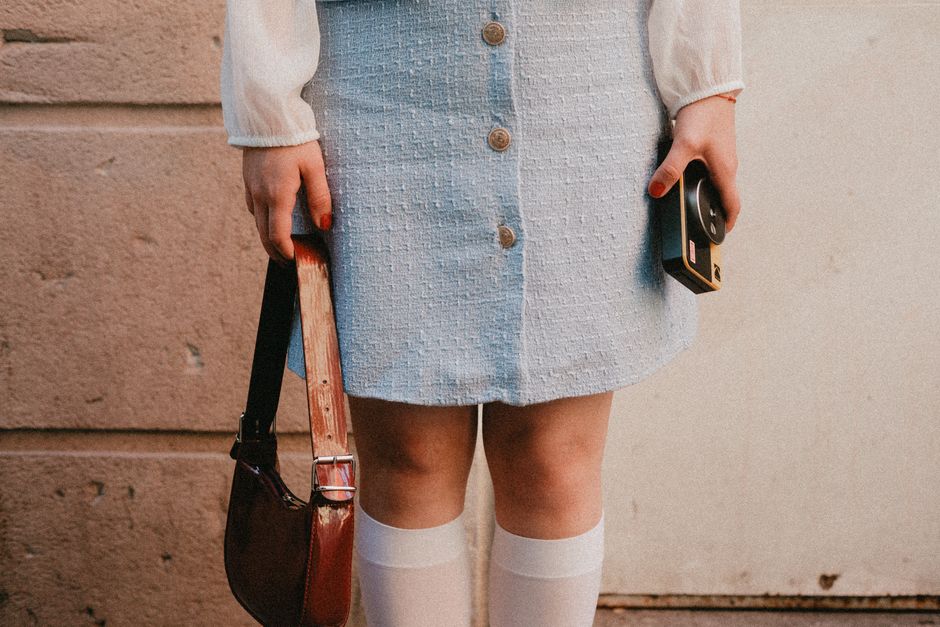 Stylish woman in retro outfit holding a vintage camera and handbag