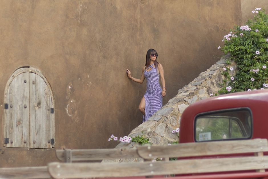 Stylish woman in sunglasses posing near a textured wall beside blooming flowers