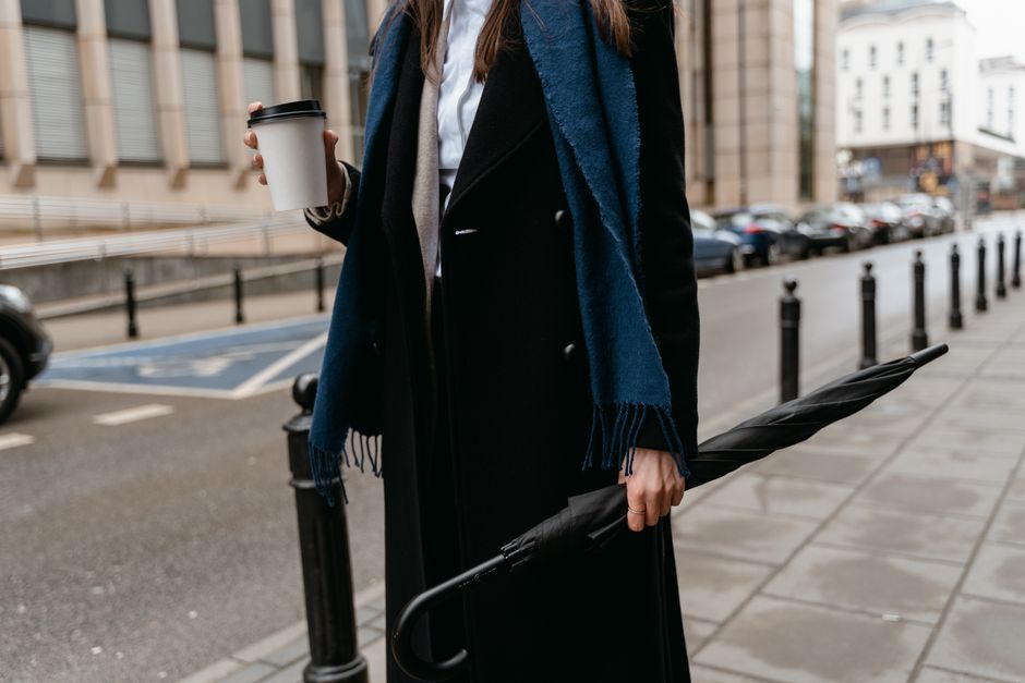 Stylish woman in urban setting with coffee and umbrella, signifying a chic city lifestyle