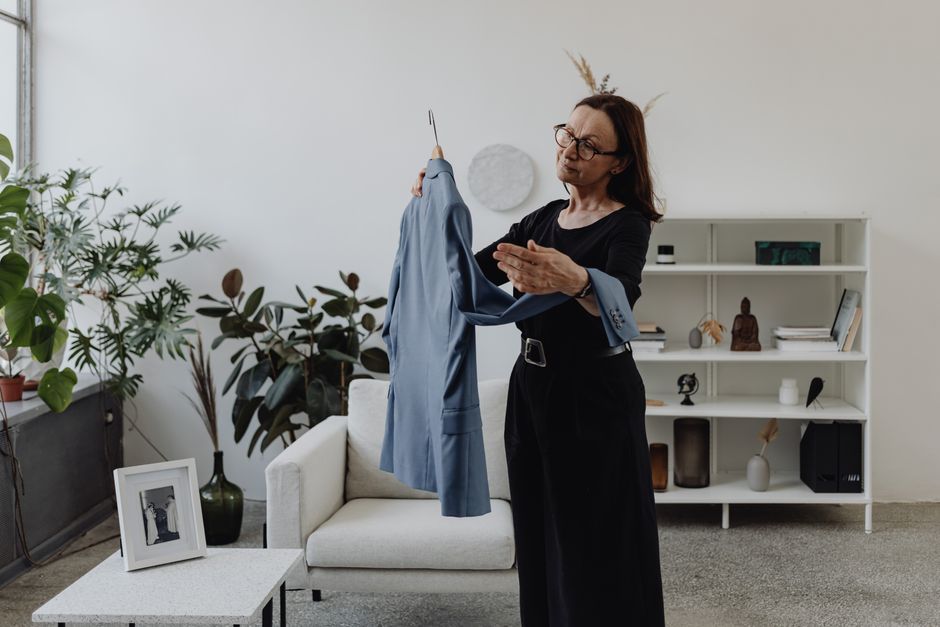 A woman in a modern living room holding a blue suit jacket pensively.