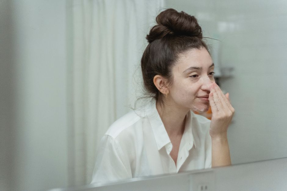 Woman applying face cream in bathroom, focusing on skincare routine with natural reflection in mirror