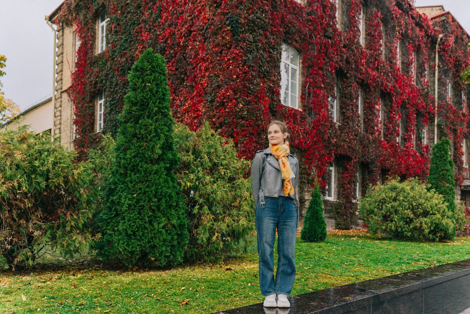 Woman in casual attire poses next to a building adorned with red ivy foliage, captured in Grodno, Belarus