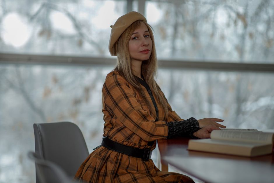Woman in plaid dress and beret reading at a table in a serene library