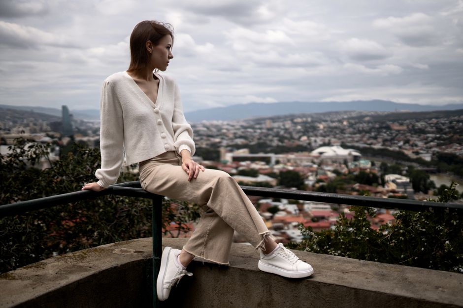 Woman sitting on a rail with city view, wearing casual outfit, serene expression