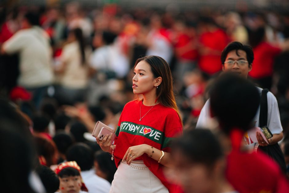 Young woman in a red shirt amidst a large outdoor crowd during the day