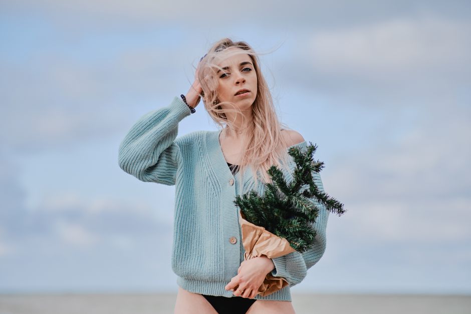 Young woman with windswept blond hair in a cardigan, holding a small Christmas tree